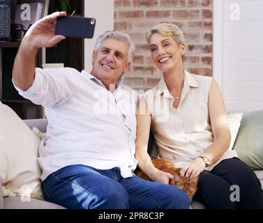 Ci siamo semplicemente rilassati. Una coppia matura ha preso dei selfie mentre si rilassava con il gatto su un divano a casa. Foto Stock