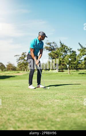 Gentilmente ora. Un giovane golfer maschio messo a fuoco circa per giocare un colpo con il suo putter su un campo da golf fuori durante il giorno. Foto Stock