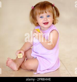 Il shes ha avuto un grande inizio nella vita. Bambina carina in un abito rosa che gioca felicemente con alcuni blocchi di legno. Foto Stock