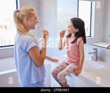 La giovane madre caucasica e la sua bambina si lavano i denti con gli spazzolini al mattino.insegnare ai bambini le basi di una buona igiene orale Foto Stock