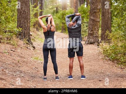 Tutta la lunghezza di un giovane atleta maschile e femminile che si allunga prima di una corsa all'aperto in natura da dietro. Due sportivi in forma che fanno esercizi di riscaldamento nella pineta in una giornata di sole Foto Stock