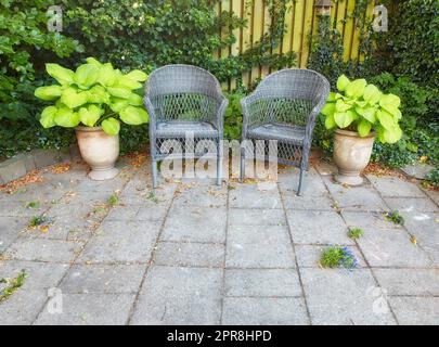 Il cortile tranquillo, sereno e invitante è ideale per rilassarsi e godersi la tranquillità. Giardino all'aperto con sedie grigie piante in vaso e pavimenti piastrellati grigi nelle giornate di sole Foto Stock