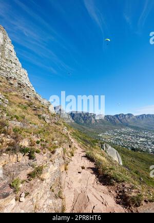 Parapendio da Lions Head con una splendida vista della Table Mountain a città del Capo, in Sudafrica. Lussureggianti alberi verdi che crescono in armonia su terreni rocciosi. Attrazione turistica per esploratori avventurosi Foto Stock