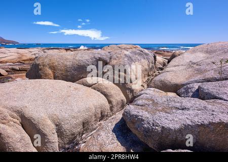 Costa rocciosa con oceano e cielo blu con copyspcae sullo sfondo. Paesaggio naturale mozzafiato o paesaggio marino di rocce. Massi o grandi pietre naturali nel mare con bellissime texture ruvide Foto Stock