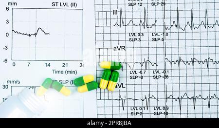 Capsule pillole verdi-gialle distribuite dal flacone di plastica bianco sulla carta per referti ECG o ECG. Effetto medico sulla funzione cardiaca. Concetto di terapia cardiaca. Farmacologia. Farmaci prescritti. Foto Stock