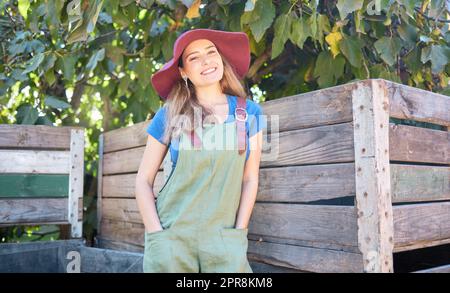 Ritratto di una giovane contadina che si gode un po' di tranquillità all'aperto in una giornata di sole. Donna felice che si rilassa dopo aver raccolto mele fresche in una fattoria sostenibile, sorridente, rilassata e tranquilla in un frutteto biologico Foto Stock