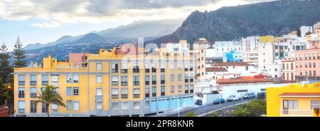 Vista panoramica di case vibranti, edifici residenziali tradizionali o strutture cittadine. Strada turistica di Santa Cruz Road, la Palma, Spagna, con montagne sullo sfondo e cielo nuvoloso Foto Stock