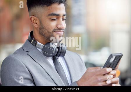 Mi piace iniziare la mia giornata con un piccolo gioco. Un bel giovane uomo d'affari in piedi in città e utilizzando il suo cellulare. Foto Stock