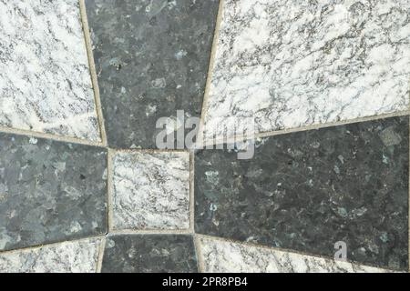 Primo piano delle piastrelle di granito nero e grigio su un pavimento. Design creativo di piastrelle in granito cementate insieme per formare un motivo incrociato. Sfondo in pietra naturale per il design degli interni Foto Stock