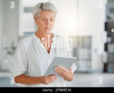 Donna d'affari matura e concentrata che tiene in mano e utilizza un tablet digitale da sola al lavoro. Una donna caucasica professionista d'affari che utilizza i social media su un tablet digitale in un ufficio al lavoro Foto Stock