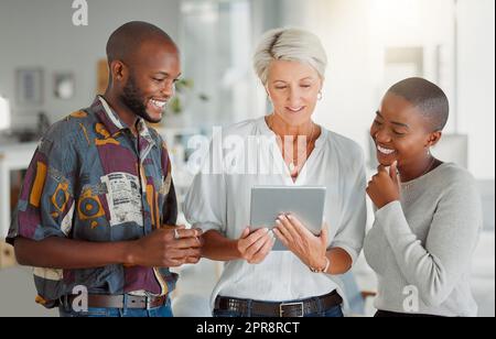 Tre persone d'affari felici che utilizzano un tablet digitale insieme al lavoro. Donna d'affari caucasica matura che parla e mostra ai suoi colleghi afroamericani l'idea di un tablet digitale in un ufficio Foto Stock