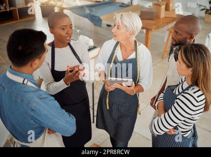 Gruppo di cinque diversi designer creativi che hanno una riunione mentre sono in piedi insieme al lavoro. Professionisti aziendali che parlano e pianificano mentre utilizzano un tablet digitale in un ufficio. Colleghi di sesso maschile e femminile che discutono di una strategia Foto Stock