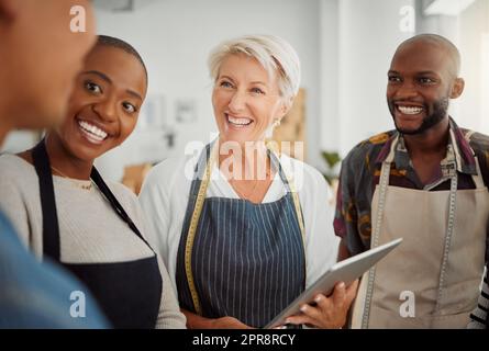 Gruppo di diversi designer creativi che hanno una riunione mentre sono in piedi insieme al lavoro. Colleghi allegri che parlano e pianificano mentre utilizzano un tablet digitale in ufficio. Colleghi di sesso maschile e femminile che discutono di una strategia Foto Stock