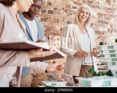 Gruppo di diversi architetti che discutono di piani, progetti e schemi durante una riunione nella sala riunioni del loro ufficio. Gli uomini d'affari fanno brainstorming e pianificano il loro prossimo sviluppo del progetto Foto Stock