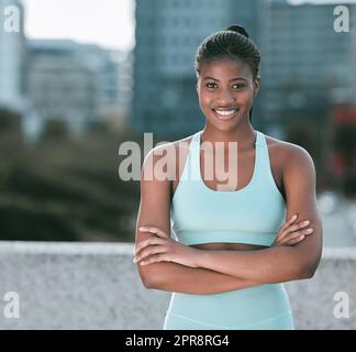 Ritratto di una giovane donna afroamericana sicura di sé, in piedi con le braccia incrociate, pronta per l'esercizio all'aperto. Atleta determinata che sembra felice e motivata ad allenarsi in città Foto Stock