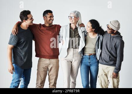 Un team di giovani uomini d'affari felici uniti che si abbracciano a vicenda. Diversi gruppi etnici misti di uomini e donne in fila nel loro ufficio, che si ammucchiano e sorridono tutti insieme. Unità e lavoro di squadra su sfondo grigio Foto Stock