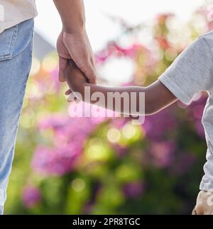 Primo piano del bambino che tiene i padri per mano con lo sfondo della natura. Famiglia afroamericana che si tiene per mano mostrando amore, sostegno e affetto. Un genitore dà una guida a un bambino e lo tiene al sicuro Foto Stock