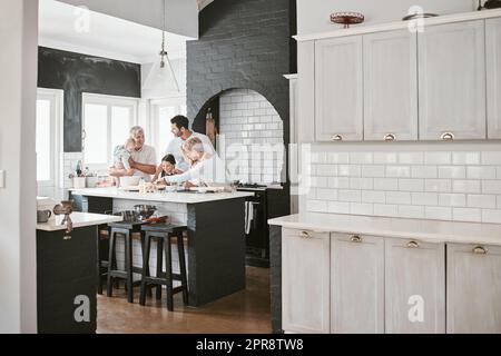 . Felice famiglia caucasica multi-generazione che prepara insieme e parla in cucina. Incollaggio prolungato in famiglia durante la miscelazione degli ingredienti per una torta. Una bambina che fa il forno con i suoi genitori e i suoi nonni. Foto Stock