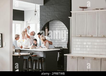 . Felice famiglia caucasica multi-generazione che prepara insieme e parla in cucina. Incollaggio prolungato in famiglia durante la miscelazione degli ingredienti per una torta. Una bambina che fa il forno con i suoi genitori e i suoi nonni. Foto Stock