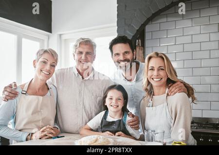 . Una famiglia caucasica felice e sorridente che fa il forno insieme in cucina. Piccola ragazza allegra che aiuta i suoi genitori e i suoi nonni a cuocere. Donna e uomo anziano che cucinano con la loro famiglia. Foto Stock