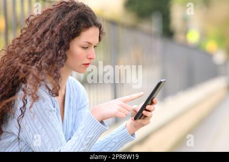 Donna seria che usa il cellulare seduta per strada Foto Stock