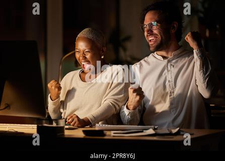 Abbiamo segnato un grande tempo: Due uomini d'affari che si acclamano mentre lavoravano su un computer in ufficio di notte. Foto Stock