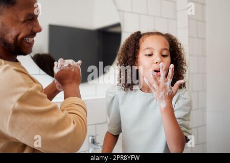 Buon padre e figlia di razza mista che si lavano le mani insieme in un bagno a casa. Un genitore afroamericano single insegnava a sua figlia l'igiene, divertendosi e divertendosi Foto Stock