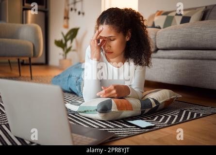 Giovane donna stressata che usa il suo notebook. Giovane donna che soffre di mal di testa davanti al suo computer. I problemi dei notebook si verificano sempre a casa. Donna sdraiata sul pavimento che sembra preoccupata Foto Stock