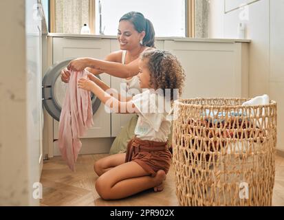 La giovane madre ispanica e sua figlia cercavano bucato sporchi nella lavatrice di casa. Adorabile bambina e sua madre che fanno le faccende insieme a casa Foto Stock