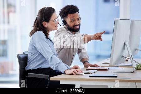 Giovane agente di telemarketing del call center caucasico che discute di piani con un collega di razza mista su un computer in un ufficio. Soluzione di risoluzione dei problemi di due consulenti per l'assistenza clienti e l'assistenza alle vendite Foto Stock