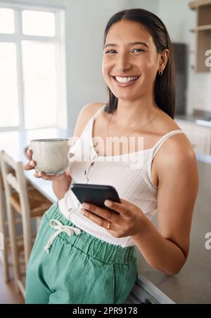 Caffè e una buona connessione wi-fi sono tutto ciò di cui hai bisogno. Una donna che tiene il cellulare mentre beve il caffè a casa. Foto Stock