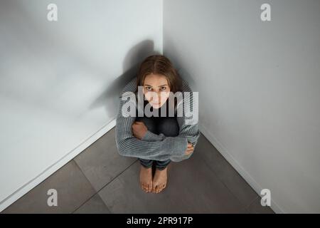 La depressione si sente così isolata. Una giovane donna depressa seduta in un angolo da sola. Foto Stock