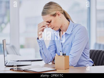 Giovane donna d'affari caucasica frustrata che lavora alla scrivania dell'ufficio soffre di mal di testa cronici mentre si siede davanti a un notebook. Donna professionale che sembra stressata e sovraccarica di lavoro Foto Stock