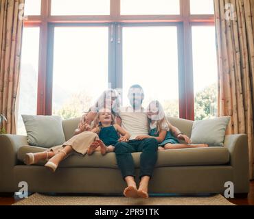 Giovane famiglia caucasica contenta felice che tiene un cartone come un tetto che li copre seduti sul pavimento a casa. Bambine allegri che legano con la madre e il padre. Genitori amorevoli che passano del tempo con le loro carine figlie Foto Stock