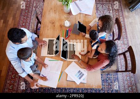 Sopra la vista i genitori che lavorano da casa con i bambini. Coppia che lavora su notebook al tavolo con figlie e figli. Famiglia che lavora a distanza e scolarizzazione a domicilio durante la pandemia di covid-19 Foto Stock