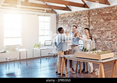 Team di ingegneri architetti soddisfatti che festeggiano insieme a un massimo di cinque dopo aver completato un piccolo modello di complesso di appartamenti su scala. Un gruppo di designer professionisti progetta un edificio per uffici Foto Stock