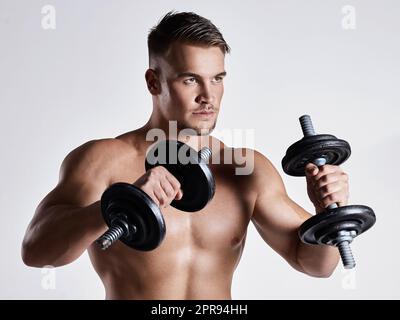 Un piccolo progresso ogni giorno si traduce in grandi risultati. Un giovane sportivo che si allena con manubri su sfondo grigio. Foto Stock