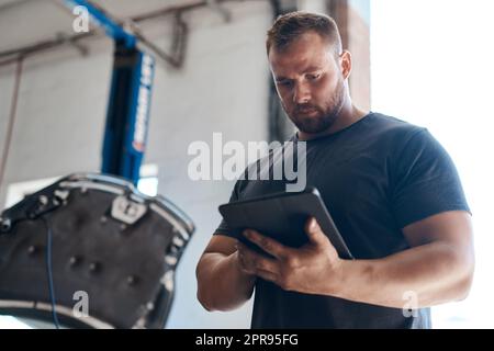 Questo strumento ci aiuta a testare le parti dell'auto senza smontare il veicolo. Un meccanico che utilizza un tablet digitale mentre lavora in un'officina di riparazione. Foto Stock