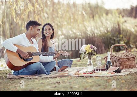 Condividere il mio amore con la musica. Scatto a tutta lunghezza di una giovane donna seduta con il suo ragazzo mentre suona la chitarra durante la loro data di picnic. Foto Stock