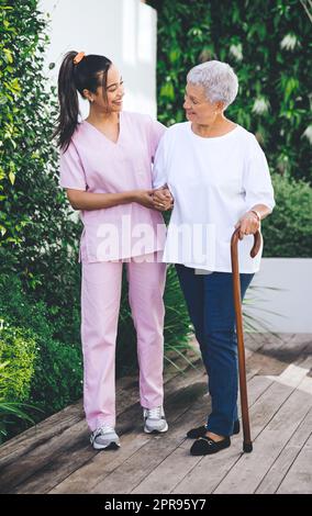 Per sempre in debito al vostro consiglio inestimabile. Una donna più anziana usando un bastone di camminata e camminare con l'aiuto di un fisioterapista. Foto Stock