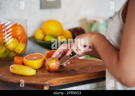 Le sostanze nutritive e il coltello si scontrano. Una donna irriconoscibile che affetta frutta e prepara la colazione in cucina a casa. Foto Stock