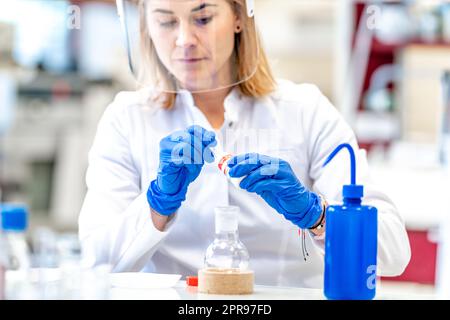 Una donna conduce ricerche sulle sostanze chimiche pericolose nel laboratorio biochimico dell'Istituto Scientifico. Utilizzare dispositivi di protezione, vetro Foto Stock