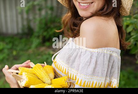 La ragazza sorride in un cappello di paglia e tiene in mano un piatto con il mais bollito. Il concetto di svago all'aperto, barbecue. Foto Stock