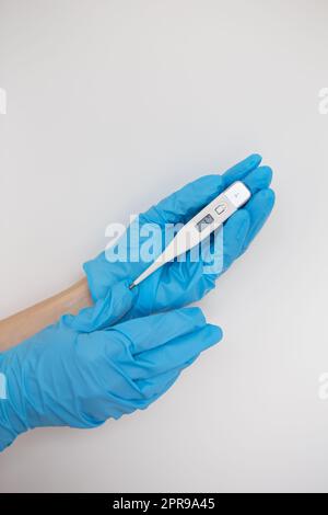 Mano del medico con un guanto in lattice blu che regge un termometro Foto Stock