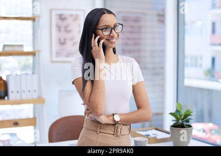 È un'ottima cosa da parlare. Una giovane donna d'affari attraente che guarda pensata mentre fa una telefonata nel suo ufficio. Foto Stock