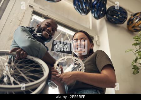 Lasciare il fissaggio a noi. Inquadratura a basso angolo di due giovani imprenditori che si trovano in piedi nel loro negozio di biciclette e che tengono in mano i pezzi di ricambio. Foto Stock