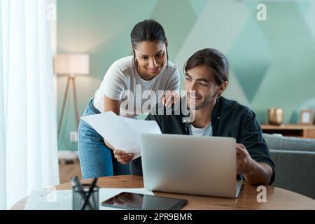 Un bell'aspetto. Una giovane coppia che fa lavoro di carta mentre usa un notebook a casa. Foto Stock