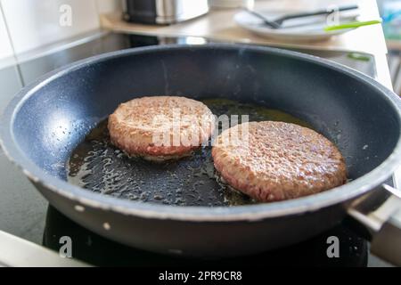 Due hamburger polpettine di carne di hamburger sfrigolante in padella calda con grassi e olio, come deliziosi hamburger fatti in casa polpette al barbecue come cibo veloce malsano pranzo con molte calorie e colesterolo in padella Foto Stock