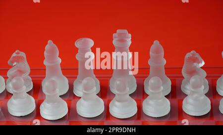 Figure di scacchi trasparenti, in posizione di partenza, su scacchiera riflettente, tono rosso. Gioco da tavolo Scacchi strategico Foto Stock