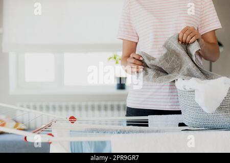 Donna che appende i capi puliti e bagnati sul piano di asciugatura nella lavanderia di casa Foto Stock